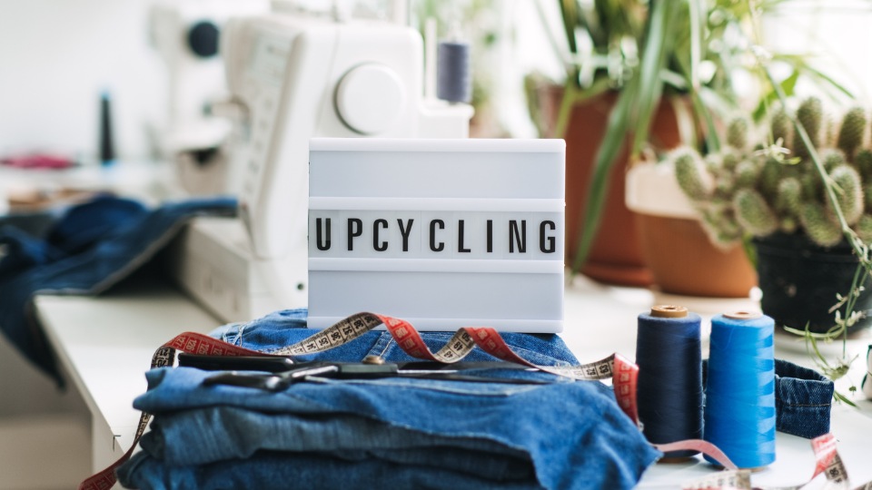 Una pila de pantalones vaqueros viejos con herramientas de costura y una caja de luz encima con el texto "UPCYCLING".