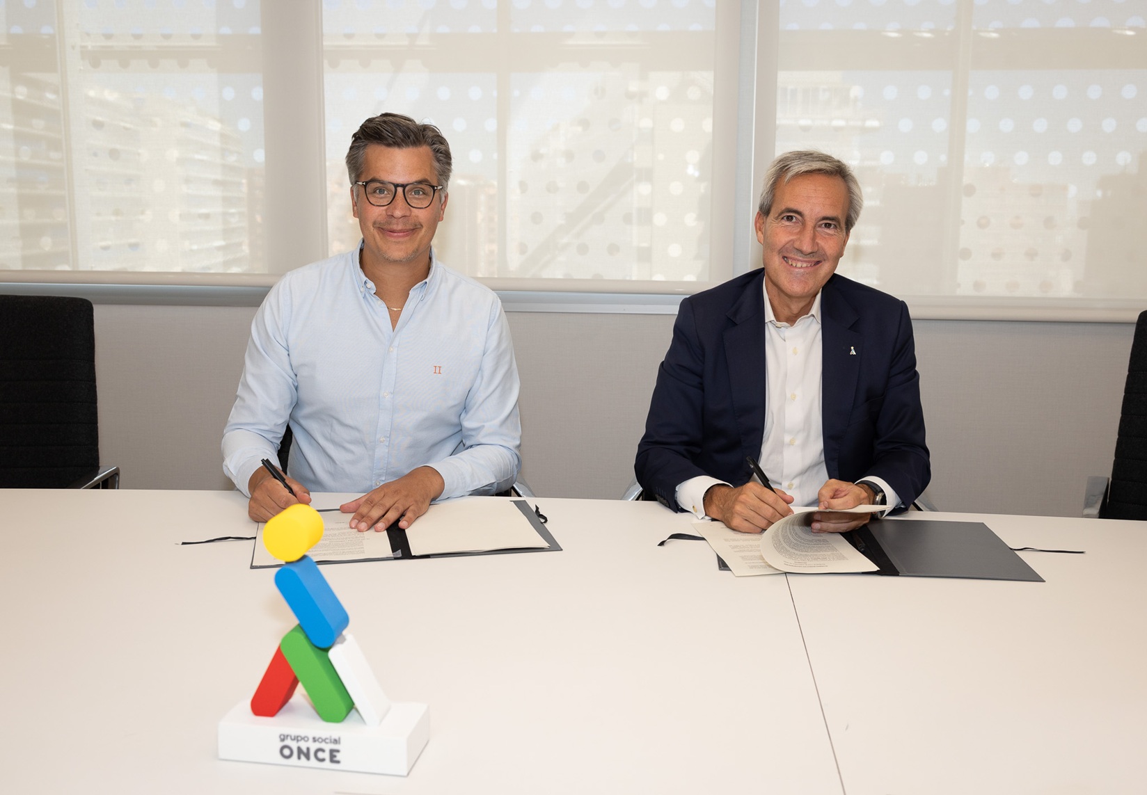 Dos representantes de IKEA y Grupo Social ONCE firman un acuerdo en una sala de reuniones, con el logotipo de Grupo Social ONCE en primer plano
