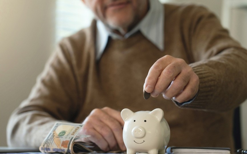 Persona colocando una moneda en una hucha blanca junto a un fajo de billetes