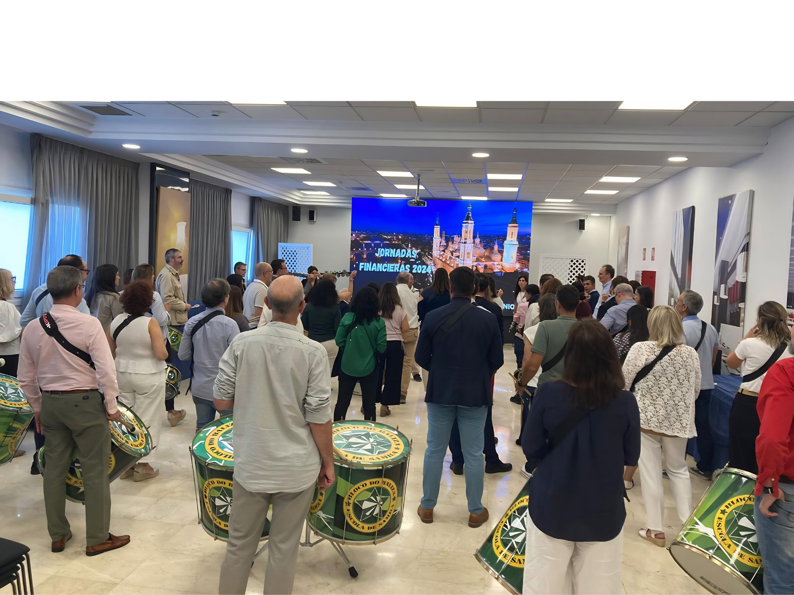 Asistentes reunidos en un salón durante las “Jornadas Financieras 2024”, con tambores en primer plano y una pantalla con el título del evento al fondo