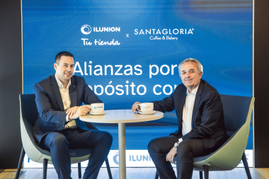 De izquierda a derecha, La firma del acuerDe izquierda a derecha, delante de un fondo azul en el que se lee 'alianzas por un propósito común', el director general de ILUNION Retail, Delio Díaz, y el presidente de FoodBox, Enrique Francia, sentados frente a una mesita con dos tazas con los logos de ILUNION y de Santagloria.
