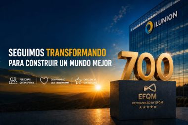 ILUNION obtiene EFQM 700; lema: “Seguimos transformando para construir un mundo mejor” frente a edificio al amanecer.