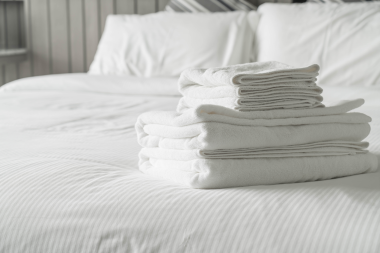 Toallas blancas dobladas sobre una cama de hotel con sábanas y almohadas blancas.