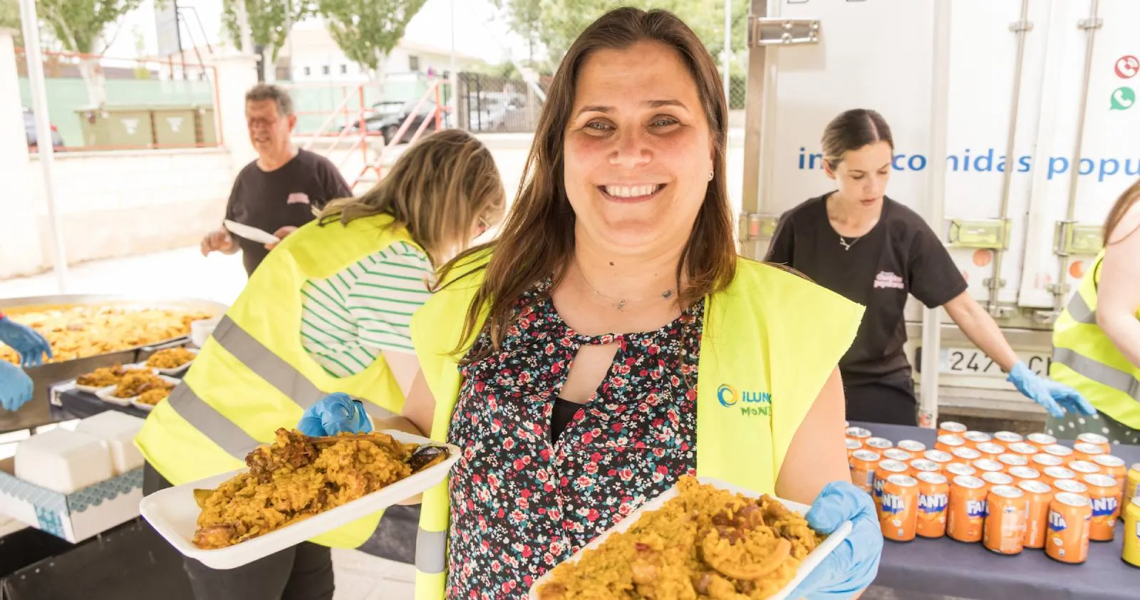 Una trabajadora de ILUNION lleva sonriente dos raciones de paella