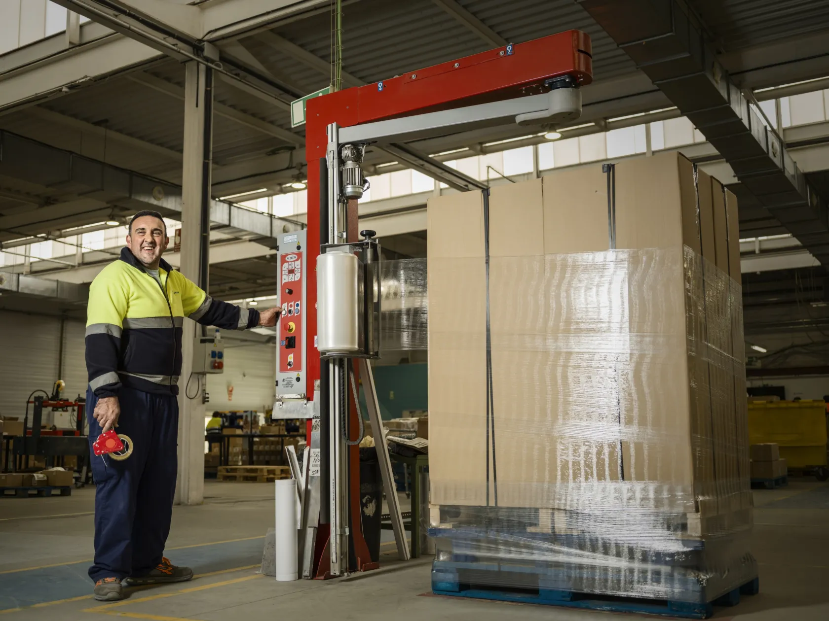 Empleado de ILUNION de pie sonriendo junto a la maquina de embalaje 