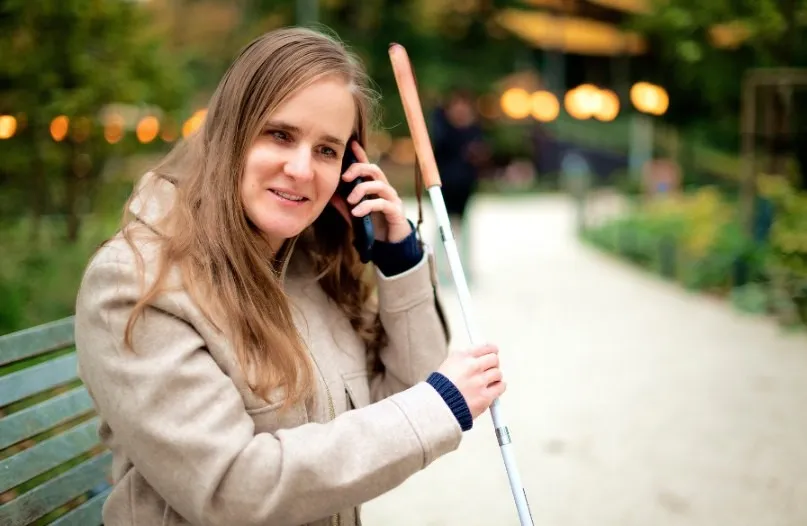 Mujer con discapacidad visual sentada en un banco utilizando el móvil