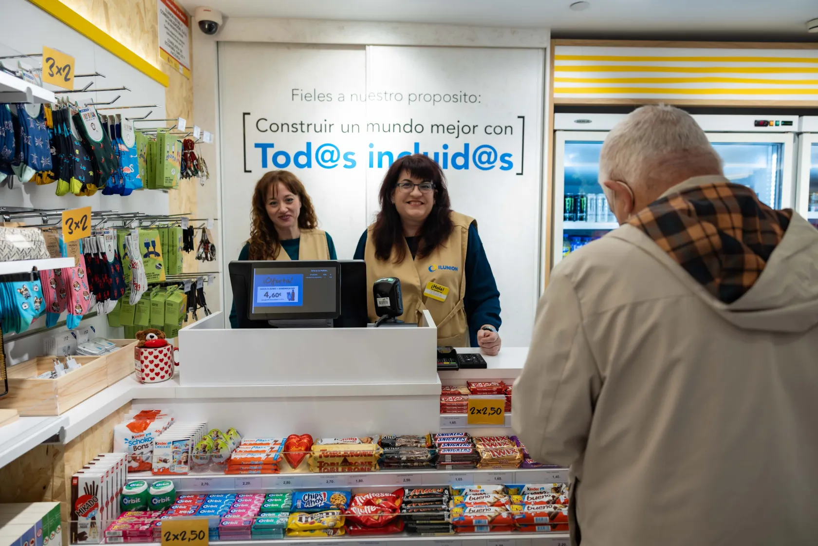 Dos de las personas que trabajan en la tienda de ILUNION Retail en el hospital Rey Juan Carlos atienden a un cliente en la caja