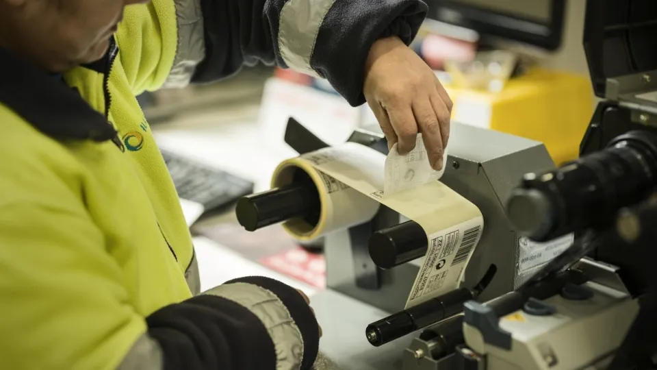 Un empleado de ILUNION con chaqueta de alta visibilidad maneja una impresora de etiquetas. 
