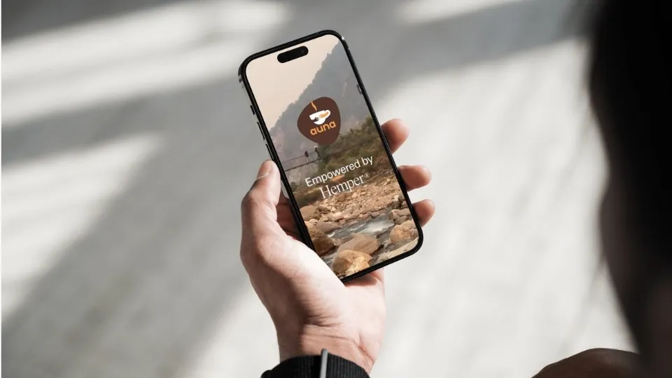 Una mano sostiene un smartphone que muestra un paisaje rocoso con el logo "auna". El texto "Empowered by Hemper" reflejando una colaboración entre ambas marcas.