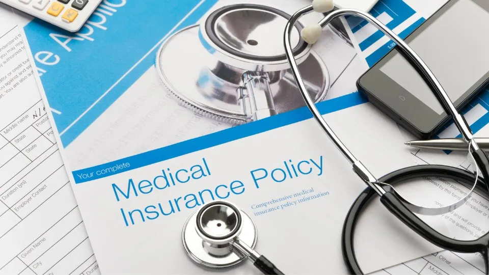 Documentos de seguro médico, un estetoscopio y un teléfono inteligente sobre un escritorio. El entorno transmite organización y planificación sanitaria.