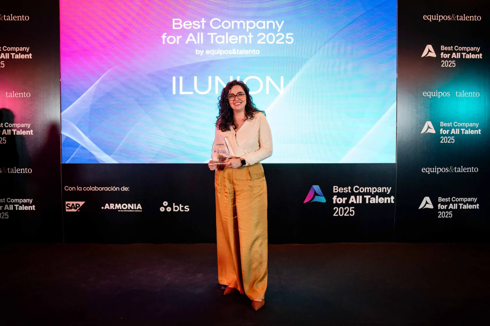 La jefa de Diversidad, Equidad e Inclusión de ILUNION, Carolina Lanchas, sostiene sonriente el reconocimiento a ILUNION como Best Company For All Talents 2025