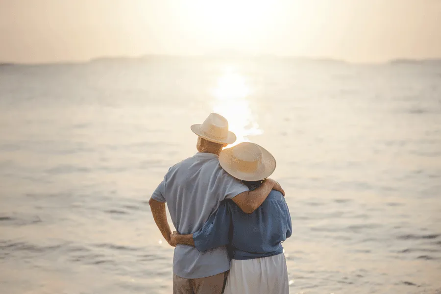 Una pareja de personas mayores en vacaciones mirando la puesta de sol en el mar