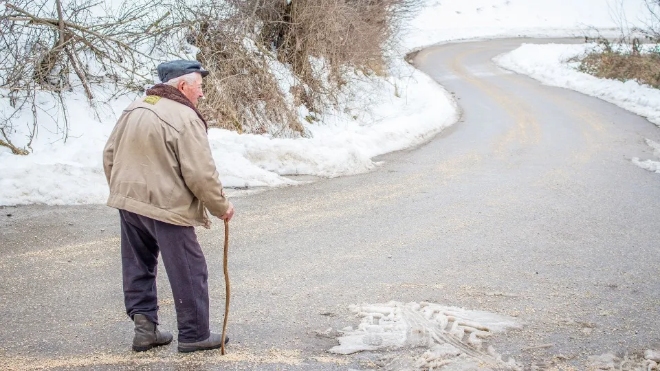 Se muestra a un anciano de espaldas con un bastón y cierta dificultad para caminar