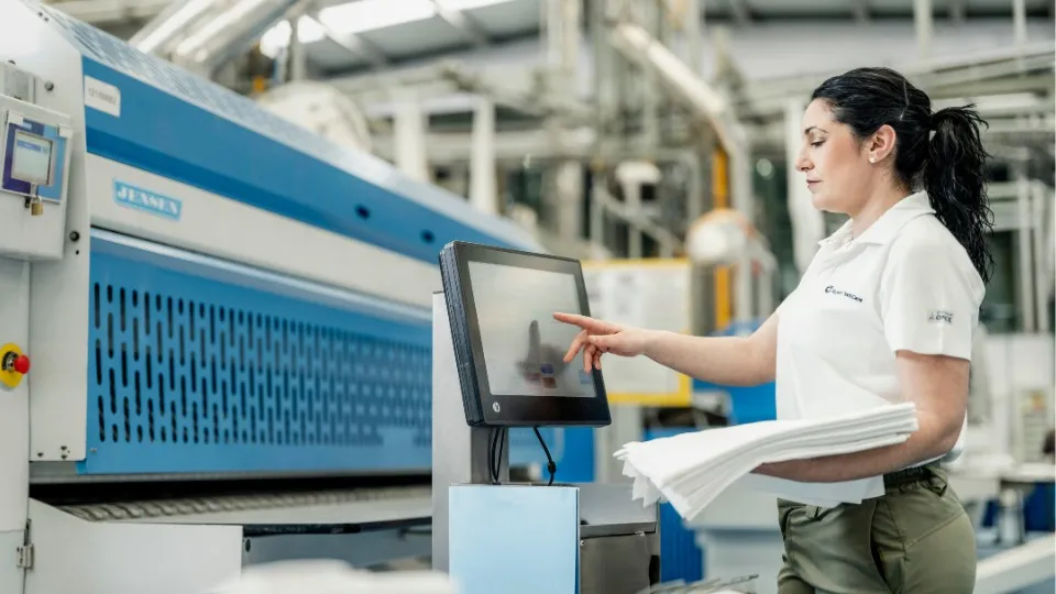 Se muestra a una trabajadora de ILUNION TextilCare con textiles en la mano y utilizando una máquina
