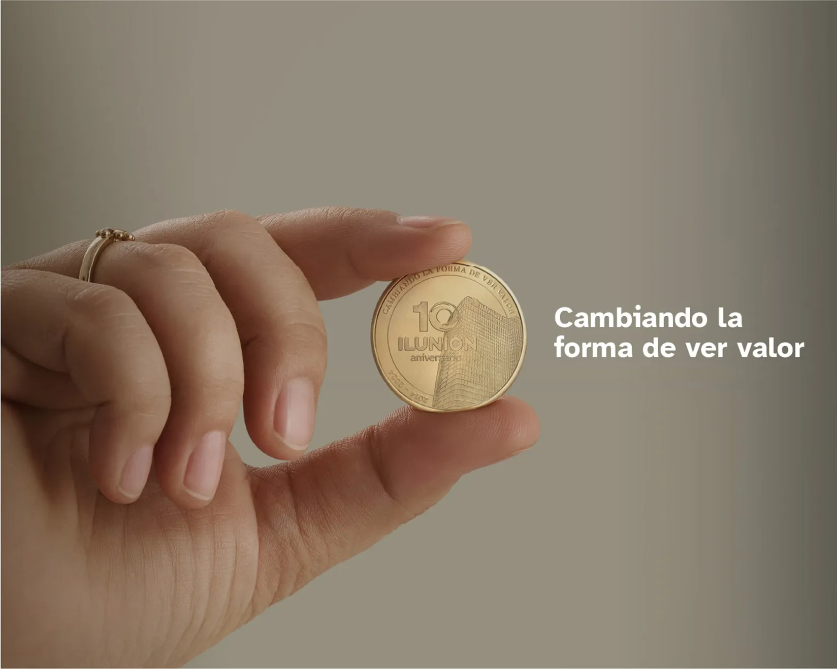 Una mano sostiene una de las monedas conmemorativas del 10 aniversario de ILUNION. A un lado se lee la leyenda: Cambiando la forma de ver valor