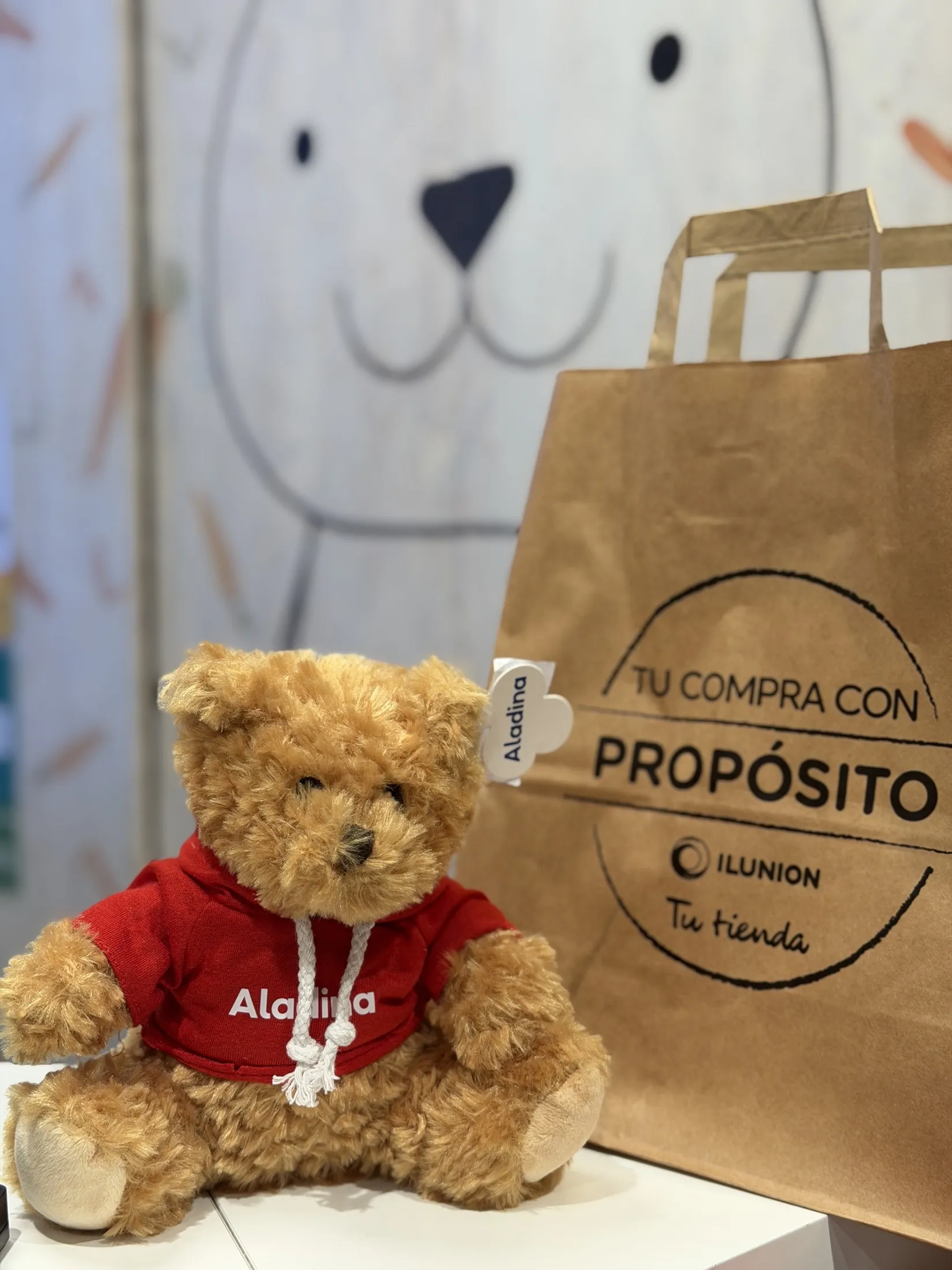Uno de los ositos de la Fundación Aladina junto a una de las bolsas de papel de ILUNION Retail