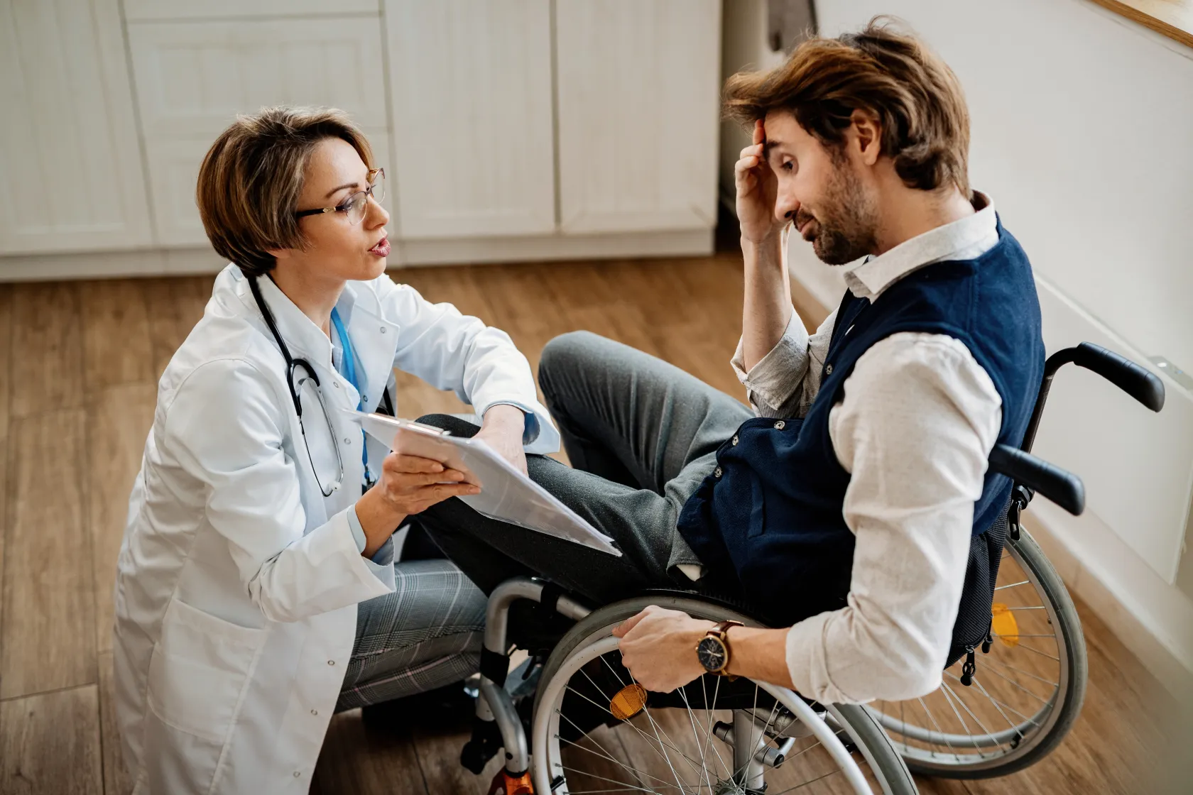 Profesional sanitario conversando con una persona usuaria de silla de ruedas en un entorno doméstico mientras revisan documentación médica