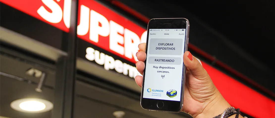 Una mano sostiene un móvil con la app beepcons frente al Supercor