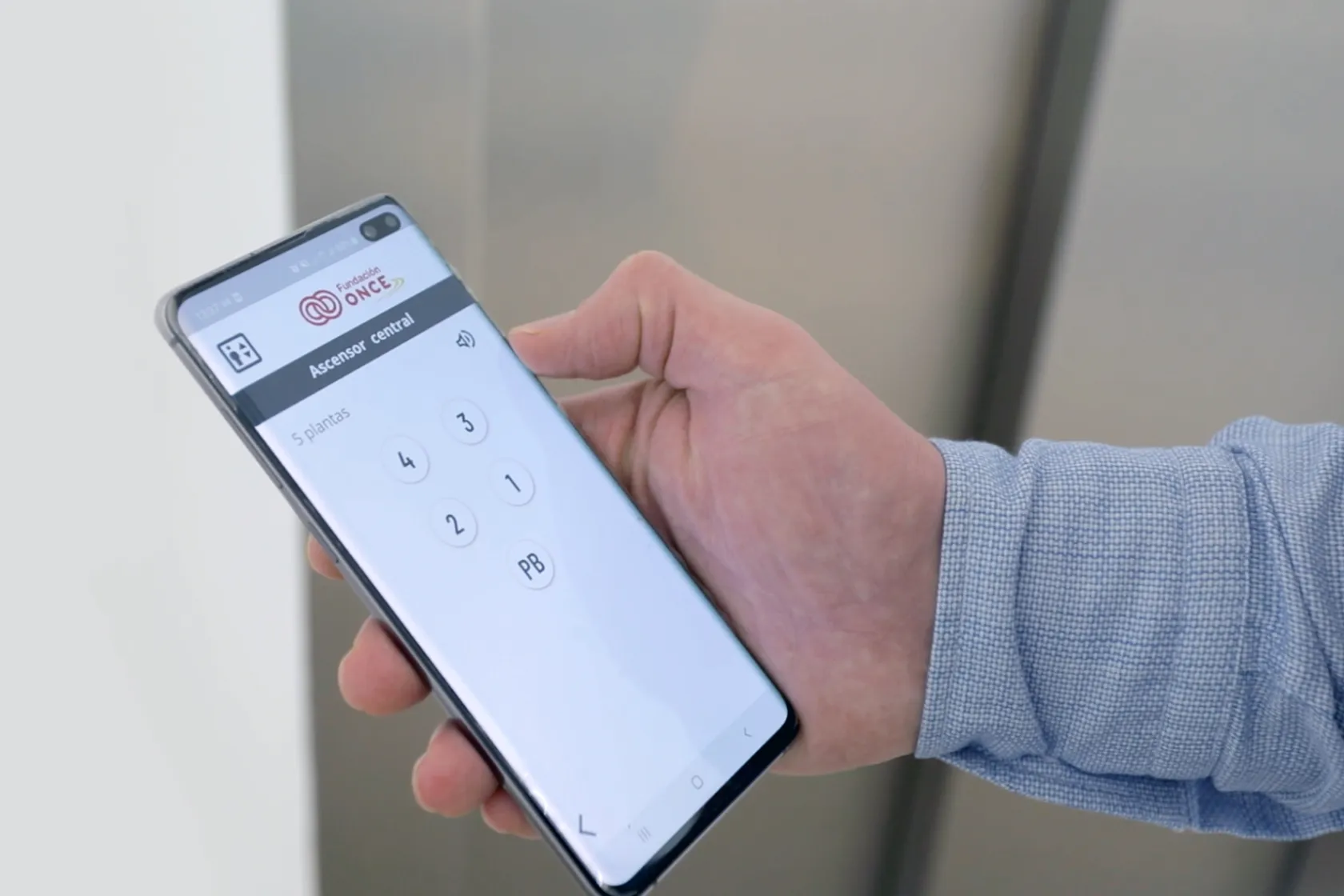 Fotografía de una mano sosteniendo un móvil en el que se ve la app de la botonera virtual