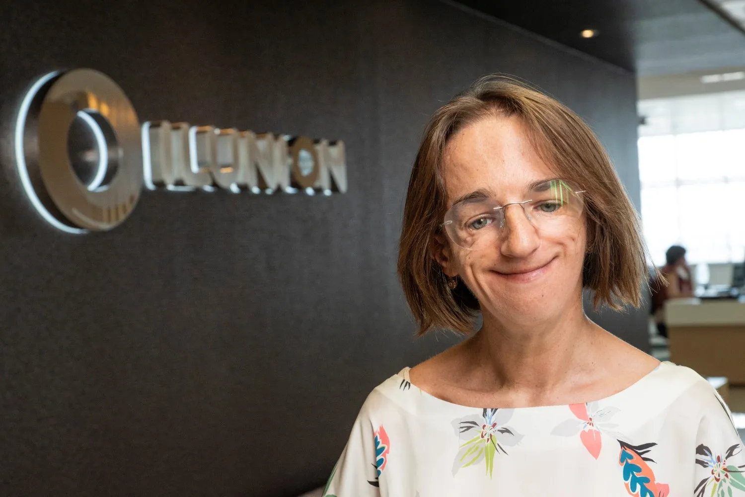 Primer plano de Vicky Bendito delante de una pared oscura donde está escrito en letras grises la palabra ILUNION