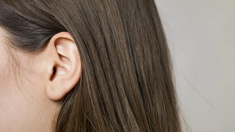 Fotografía de perfil de una mujer a la que solo se le ve una oreja y el pelo largo, liso y castaño
