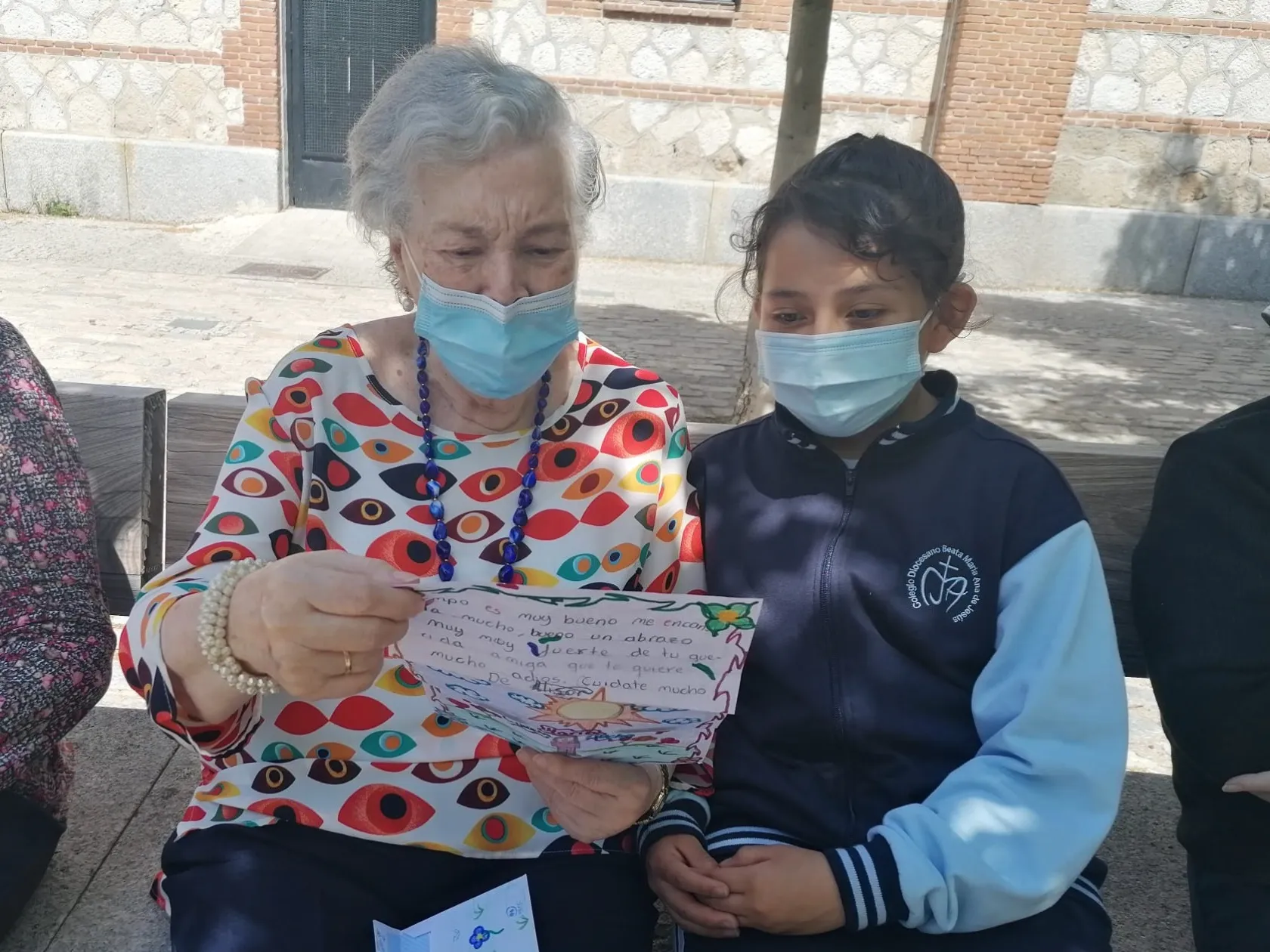 Imagen de una mujer mayor junto a un niño, ambos sostienen una carta en sus manos