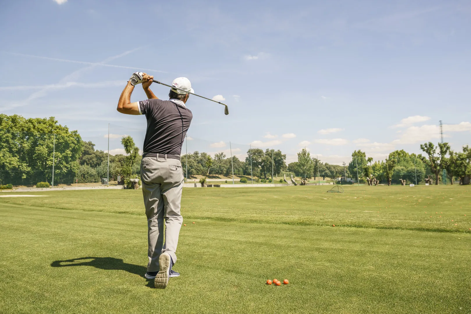 Un hombre de espaldas jugando al golf. Acaba de lanzar una pelota. 