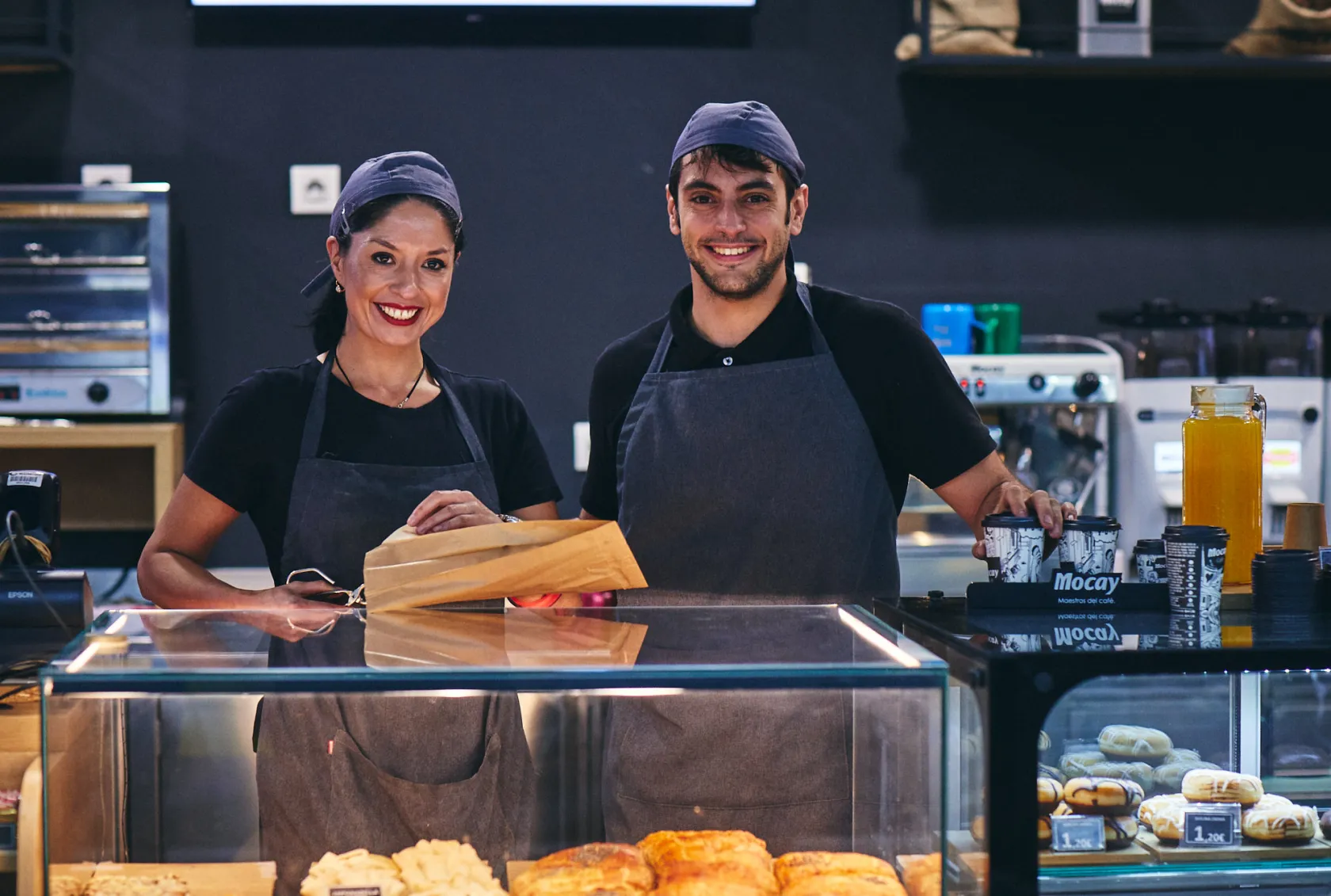 Una mujer y un hombre sonrientes detrás del mostrador de una cafetería