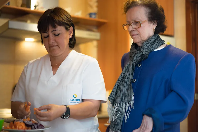 Una profesional de ILUNION pela una fruta a una mujer mayor que tiene a su lado