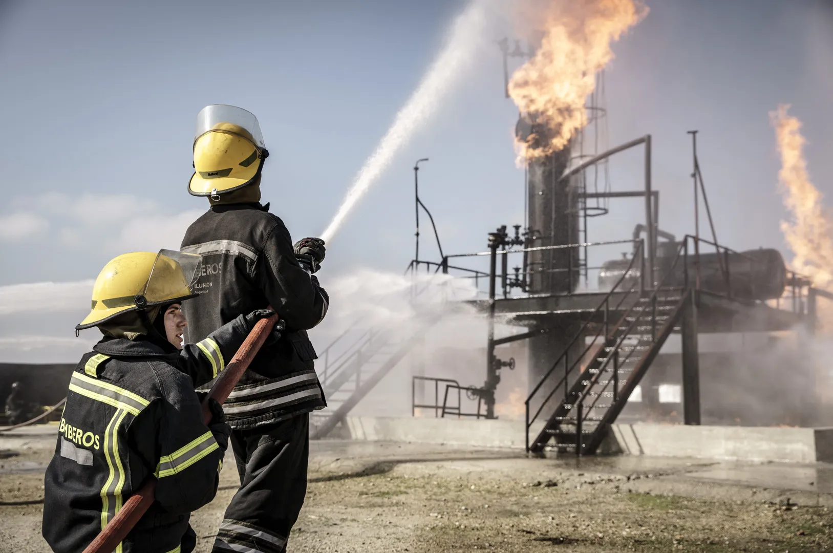 Dos estudiantes de bombero tratan de apagar  combaten el fuego en una refinería 